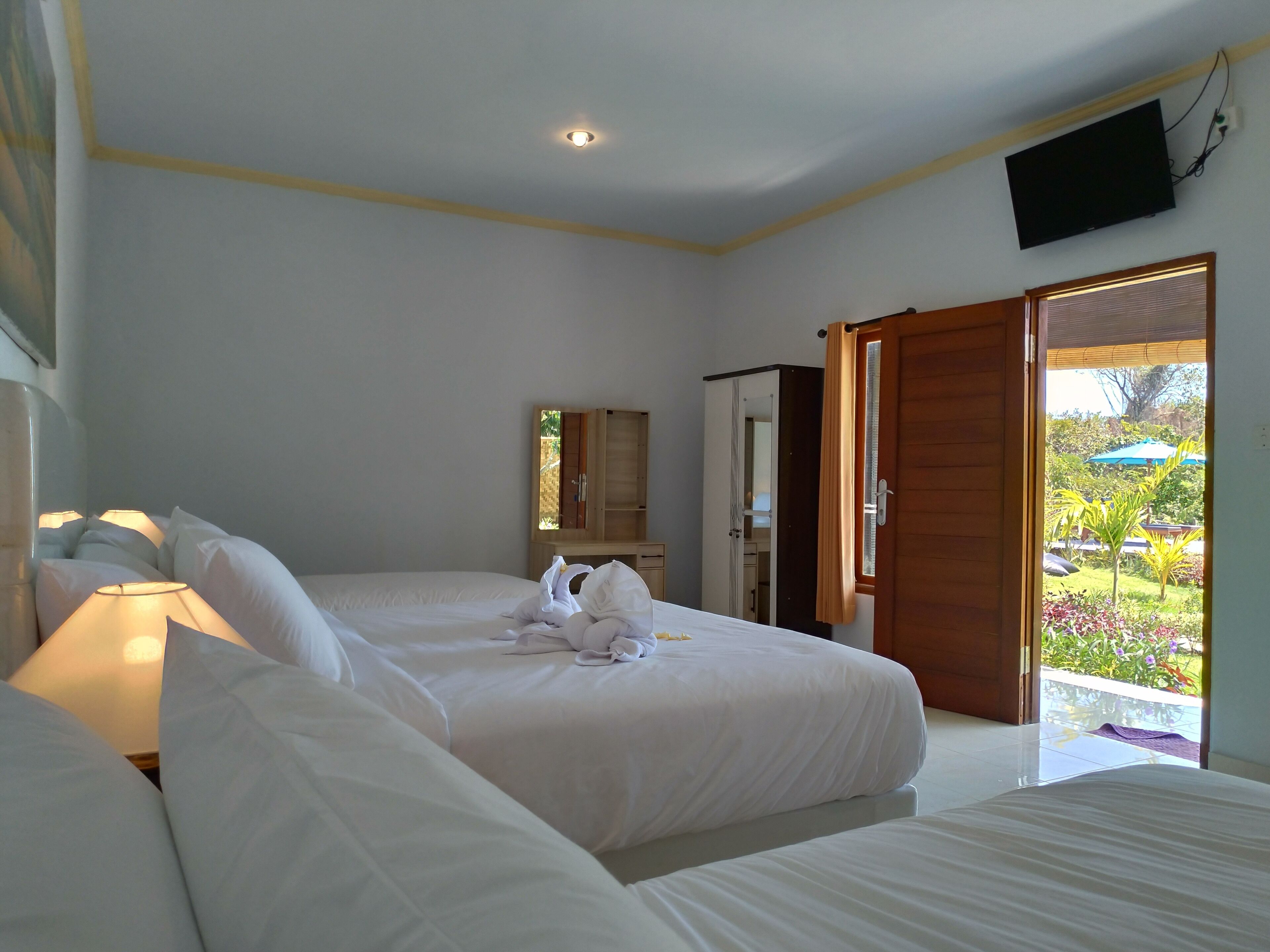 A hotel room with two beds, a television on the wall, and a door leading to a garden.