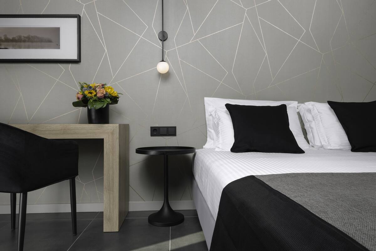 A modern hotel room with a bed, a desk, and a chair. There is a vase with flowers on the desk.