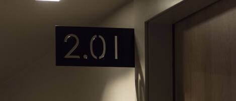 A room number sign '2.01' in a dimly lit hallway with a wooden door on the right.