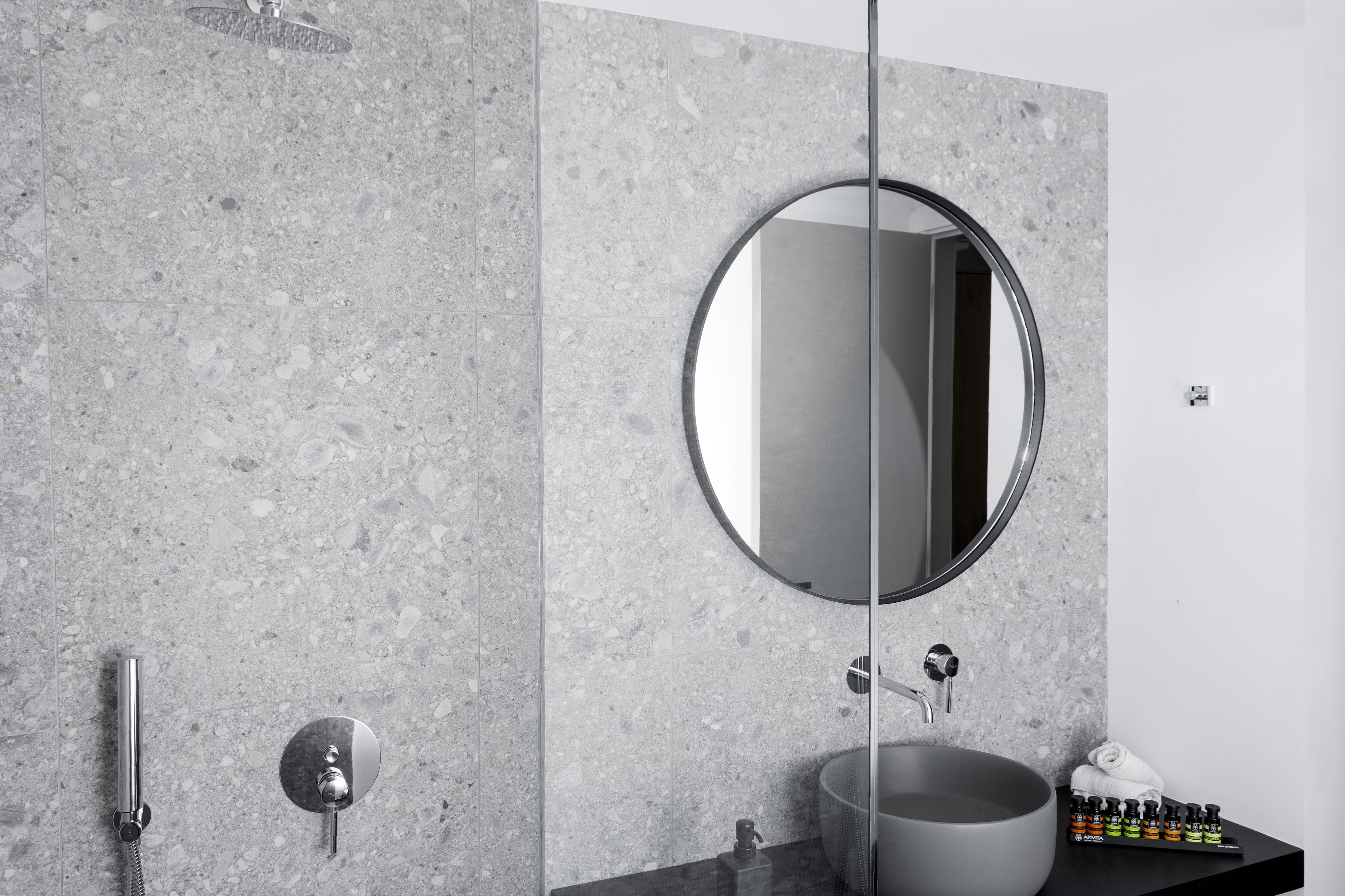 Une salle de bain moderne avec un miroir rond, un lavabo sur colonne et une douchette à main.