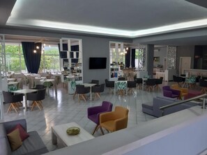 Relax in a spacious lounge area with sofas, chairs, and tables, featuring a flat-screen TV and large windows.