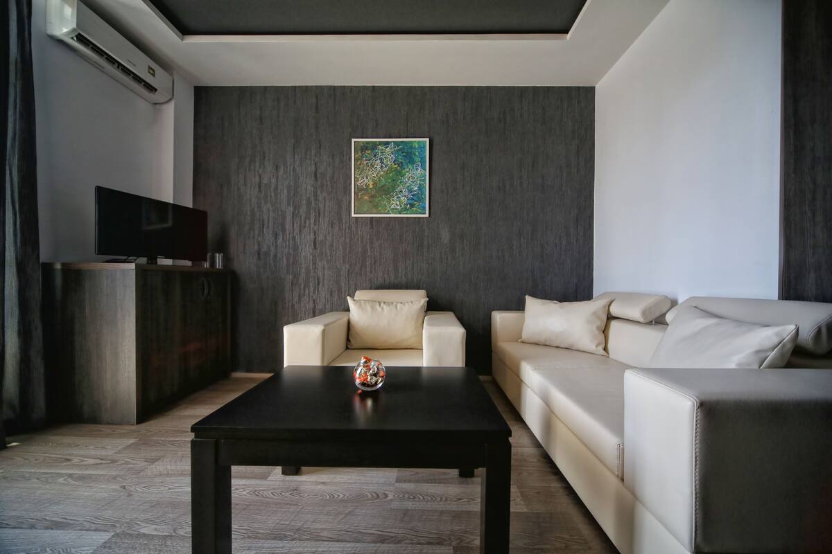 A modern living room with a dark wooden floor, a black coffee table, a beige sofa, and a TV on a wooden stand.