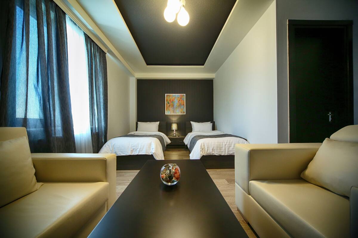 A hotel room with two beds, a coffee table, and a painting on the wall.