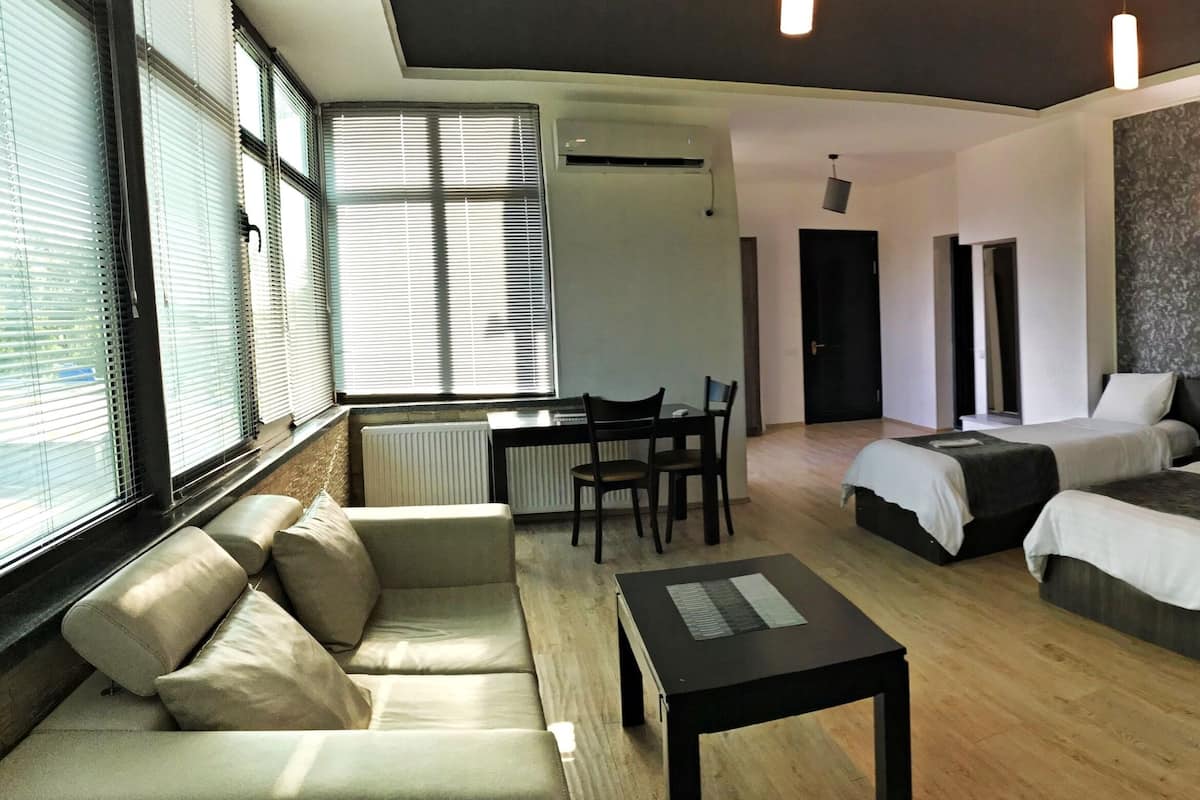 A modern hotel room with three beds, a sofa, a small table, and a desk.