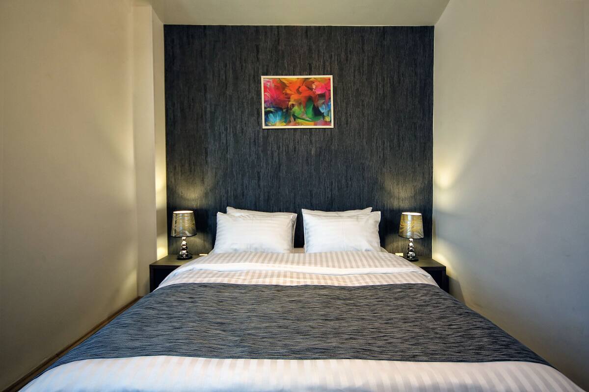 A neatly made bed with a striped bedspread, two pillows, and two bedside lamps on a dark wooden headboard.