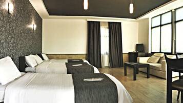 A hotel room with two beds, a sofa, a TV, and a large window with curtains.