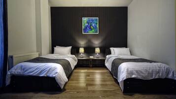 Quarto com duas camas, parede escura, um quadro e piso de madeira.