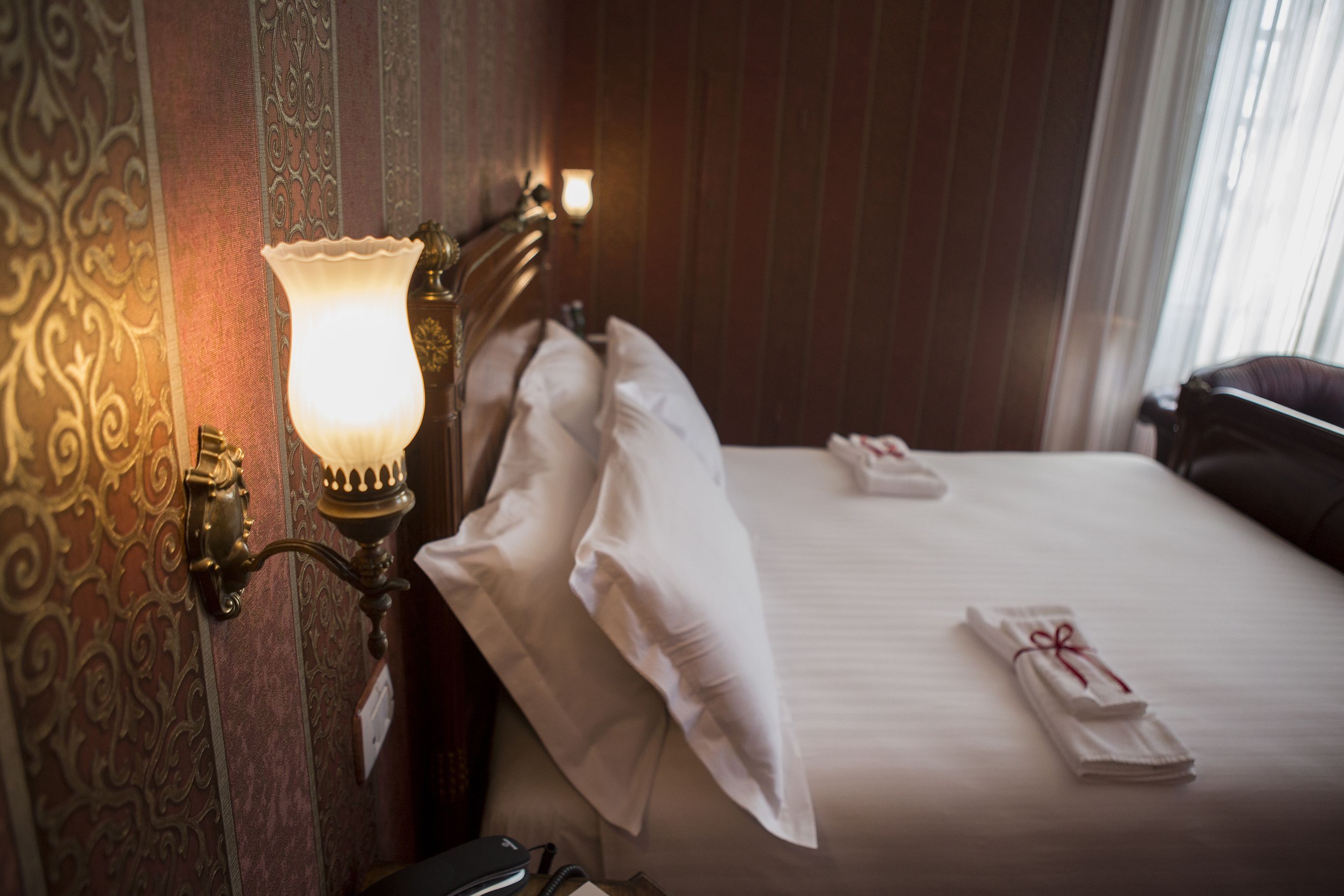 A hotel room with a neatly made bed, a wall-mounted lamp, and a decorative wall panel.