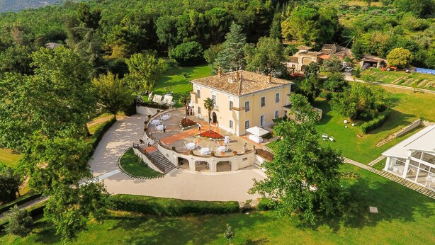 A large, single-story building with a courtyard, surrounded by lush greenery and hills.