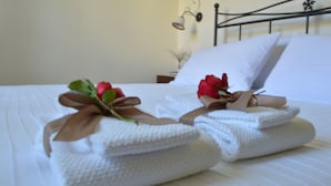 A neatly made bed with white linens and two red roses tied with brown ribbons.