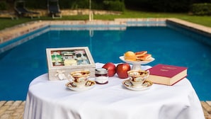 A table with tea set, apples, muffins, a book, and a candle by a pool.
