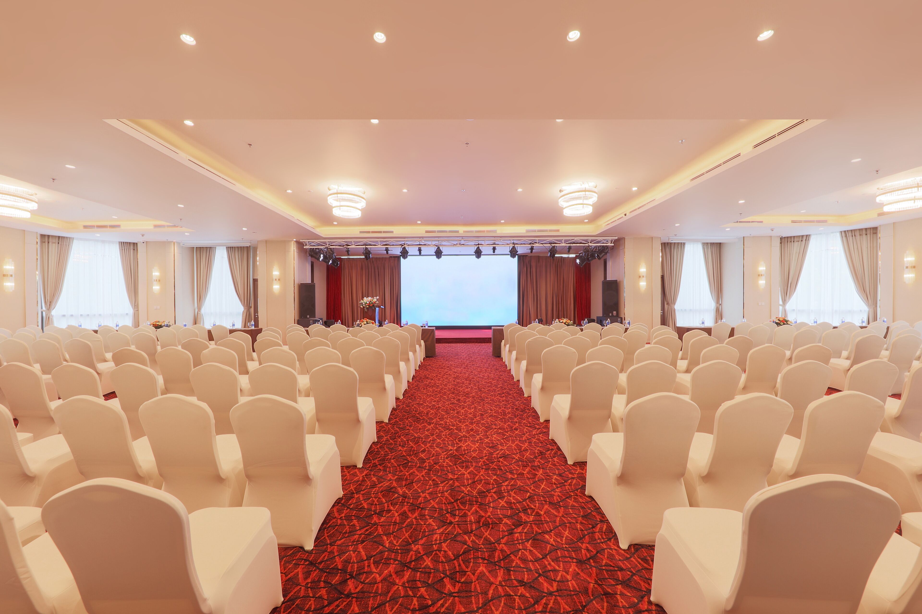 A conference room with rows of white chairs, a red carpet, and a stage with curtains.