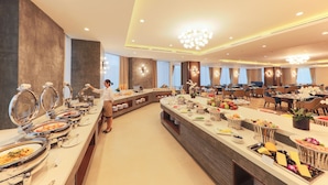 A buffet setup with various food stations, a waiter, and a spacious dining area with tables and chairs. - Grand Vista Hanoi (Hanoi)