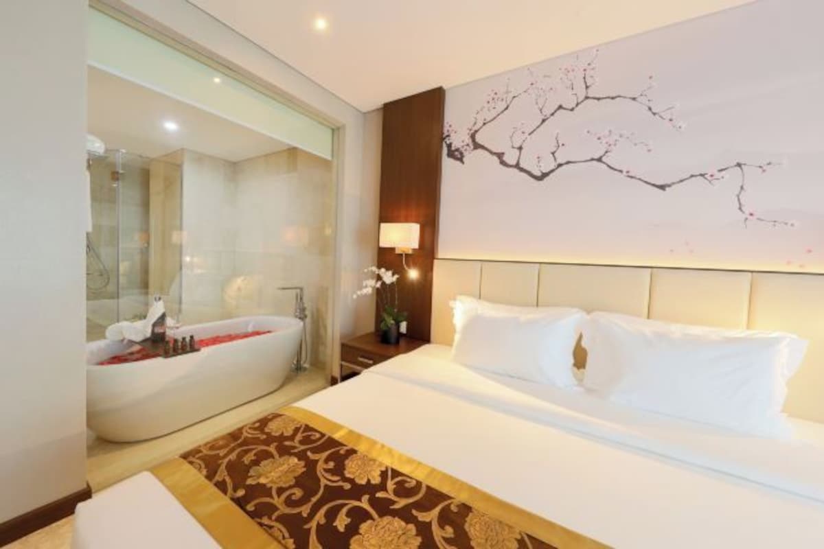 Una habitación de hotel con una cama grande, una bañera y una obra de arte colgada en la pared.