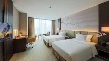 Une chambre d’hôtel avec deux lits, un bureau, une chaise, une petite table et une grande fenêtre avec des rideaux.