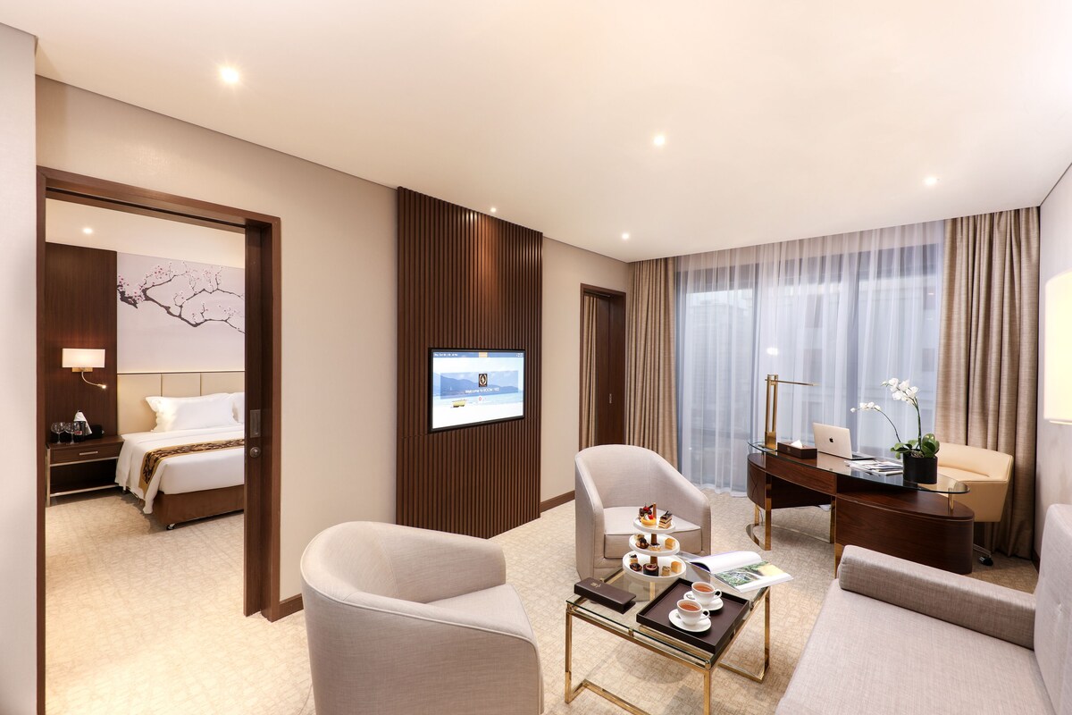 Habitación de hotel con cama, escritorio, silla, sofá, mesa de centro y televisión.