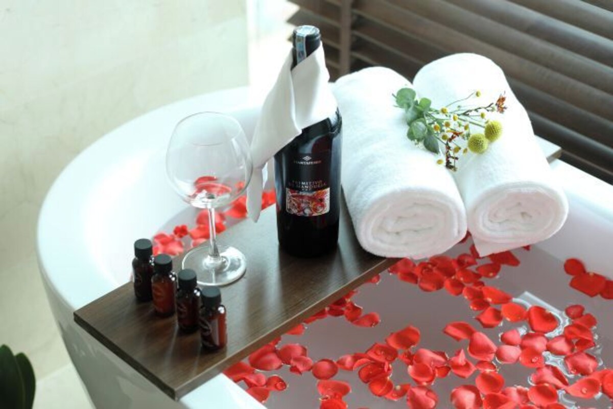 Un baño con una bañera llena de pétalos de rosa, una botella de champú, un vaso y toallas dobladas.