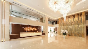 A spacious lobby with a high ceiling, a modern reception desk, and a decorative chandelier. - Grand Vista Hanoi (Hanoi)