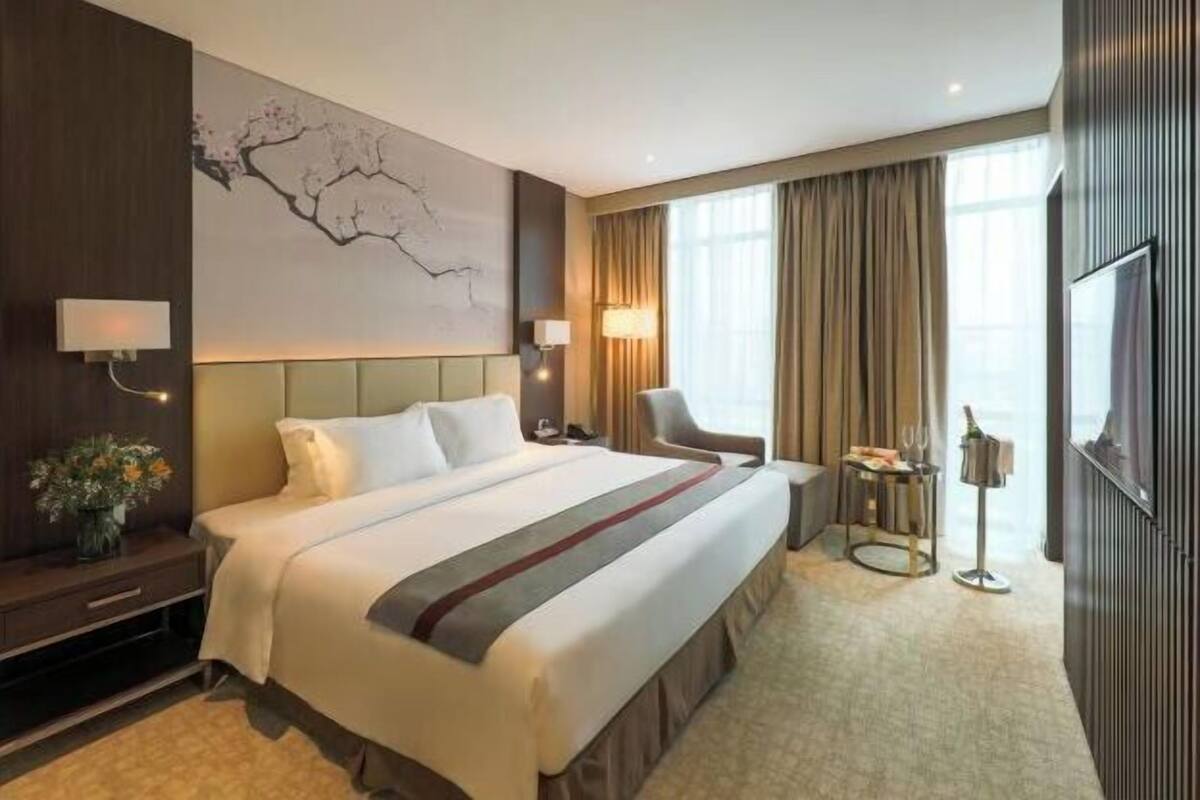 A hotel room with a large bed, a desk, a chair, a TV, and a painting on the wall.