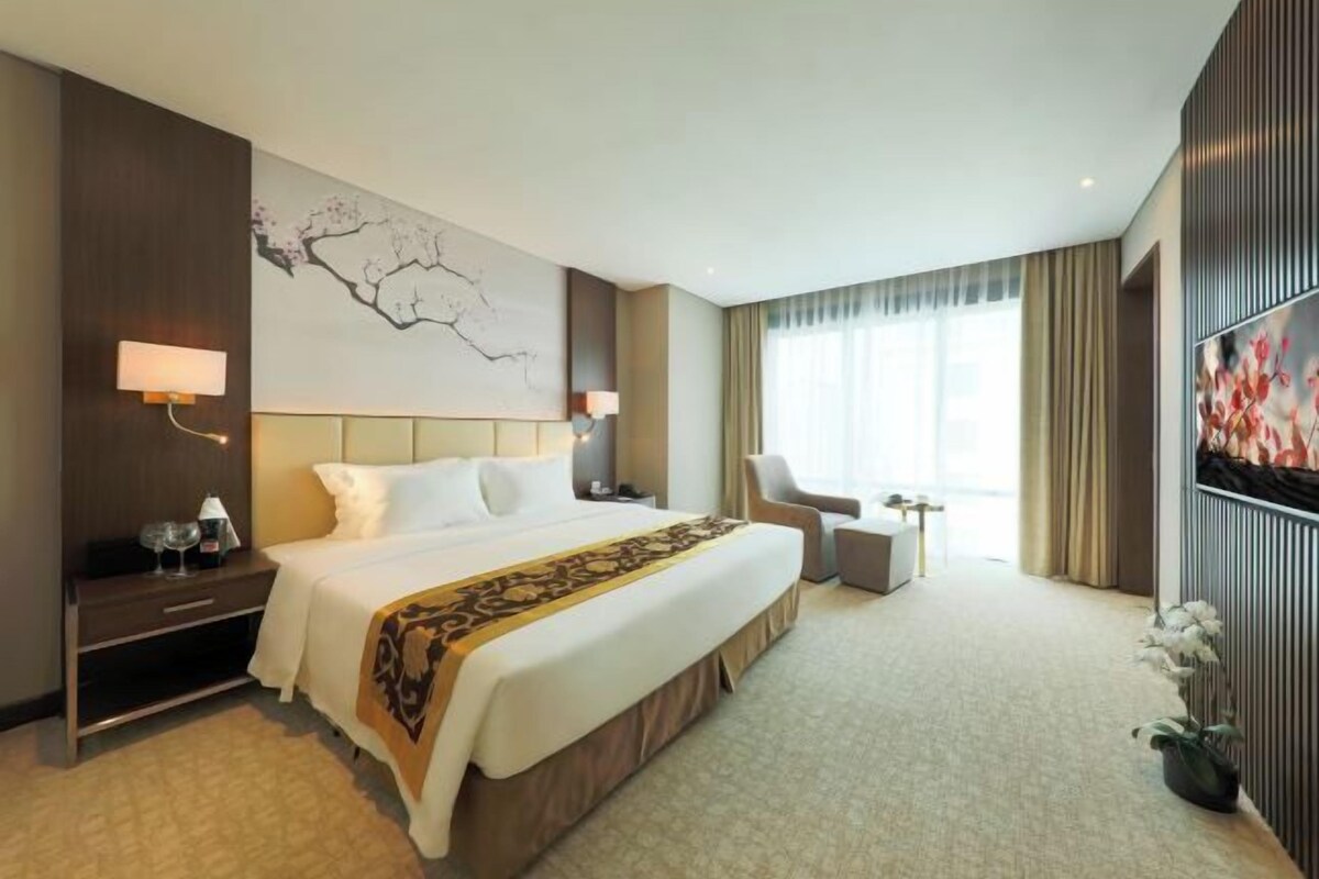 Una habitación de hotel con una cama grande, un escritorio, una silla, un televisor y una ventana con cortinas.