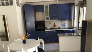 A kitchen with blue cabinets, a white dining table with chairs, and a tiled floor.