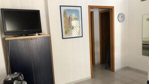 A room with a flat-screen TV on a wooden cabinet, a framed picture on the wall, a clock, and a door leading to another room.