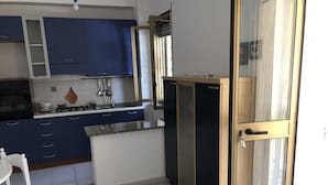 A compact kitchen with blue cabinets, a white countertop, and a small dining area with a white table and chair.