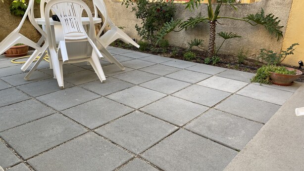 A patio area with square stone tiles, white plastic chairs, and a small palm tree.