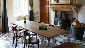 Un coin repas rustique avec une table en bois, des chaises et un banc. On aperçoit une cheminée au fond.
