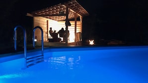 Une piscine avec une terrasse en bois et un espace salon abrité.