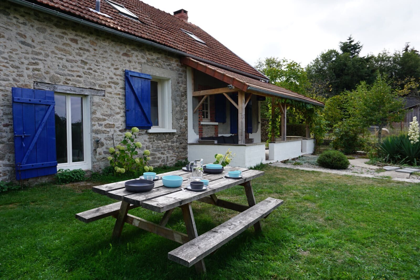 A stone house with a wooden porch and a picnic table set up outside.