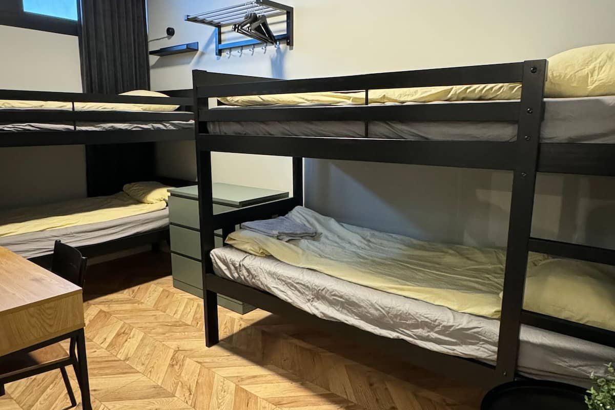 Et sovesalværelse med køjesenge, et skrivebord, en stol, en radiator og et vindue med gardiner.