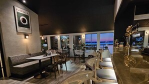 A modern restaurant with a bar area, seating arrangements, and a view of the sunset over the water. - Kallhällsbaden Vandrarhem - Hostel (Jarfalla)