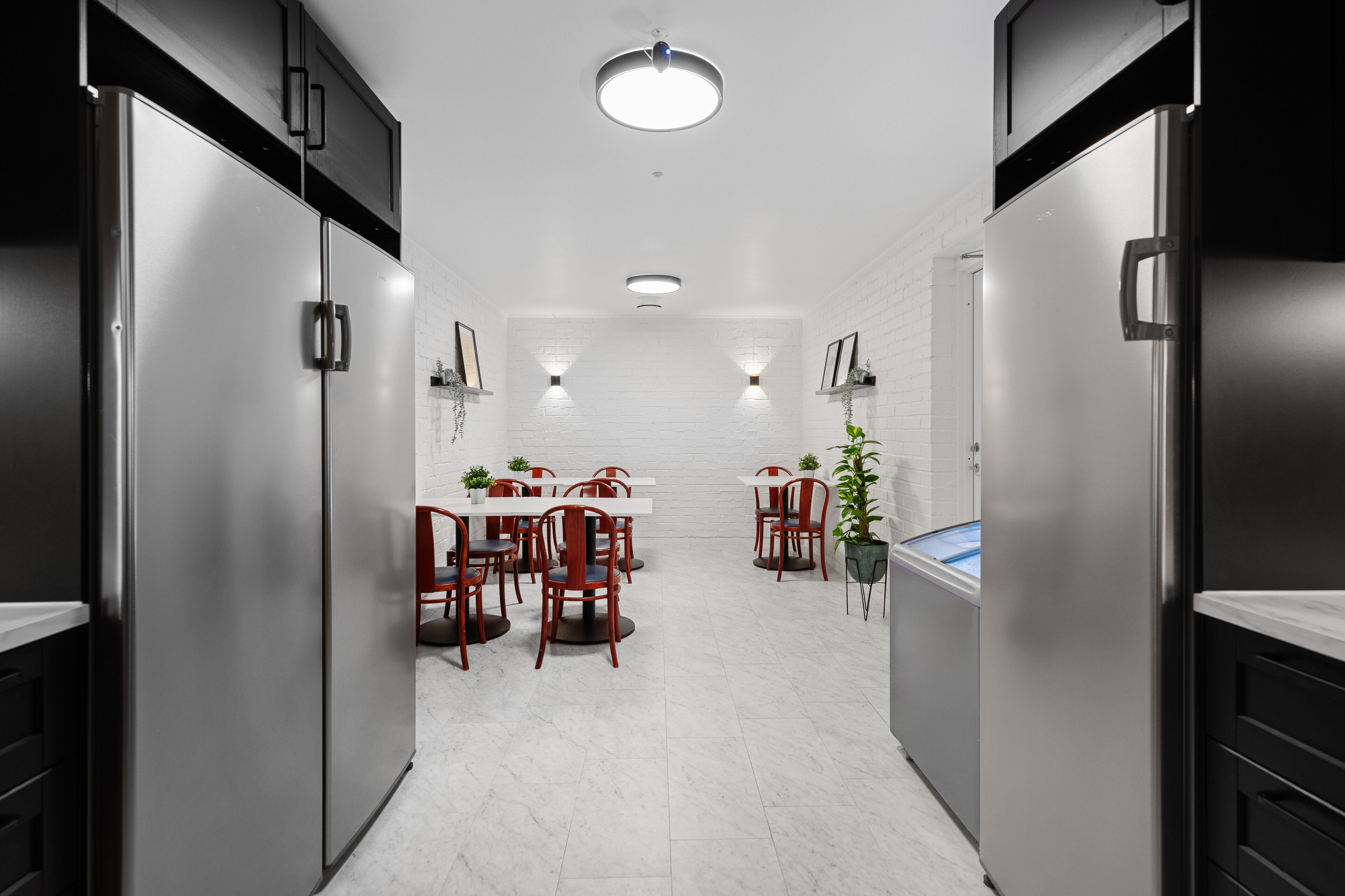 A modern kitchen with stainless steel appliances, white tiled walls, and a central dining area with red chairs and a white table.
