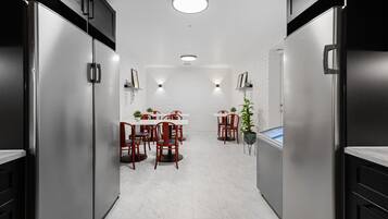 A modern kitchen with stainless steel appliances, white tiled walls, and a central dining area with red chairs and a white table.