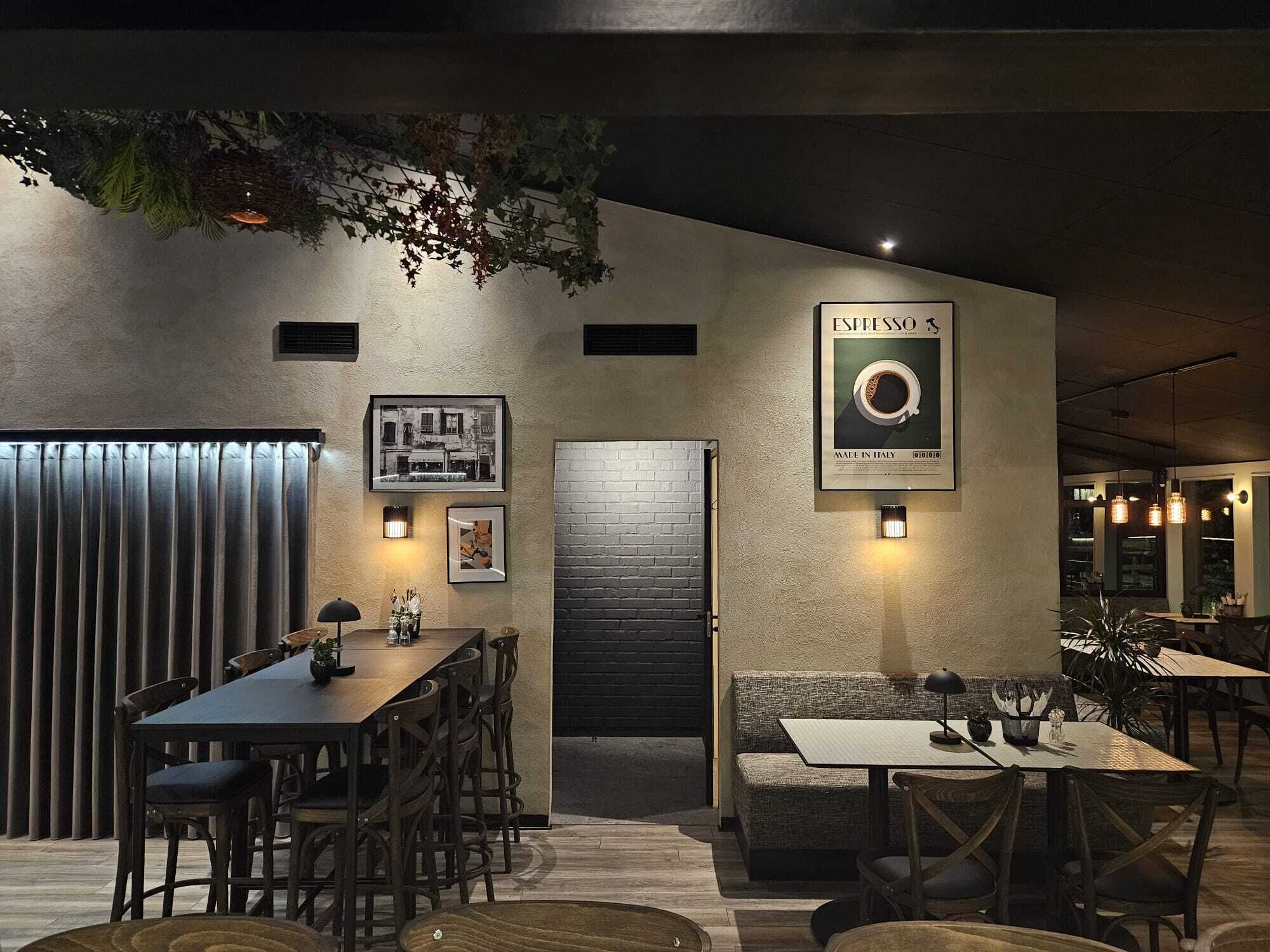 L’intérieur chaleureux du restaurant est agrémenté d’une longue table, d’un canapé et d’une enseigne publicitaire pour expresso fixée au mur.