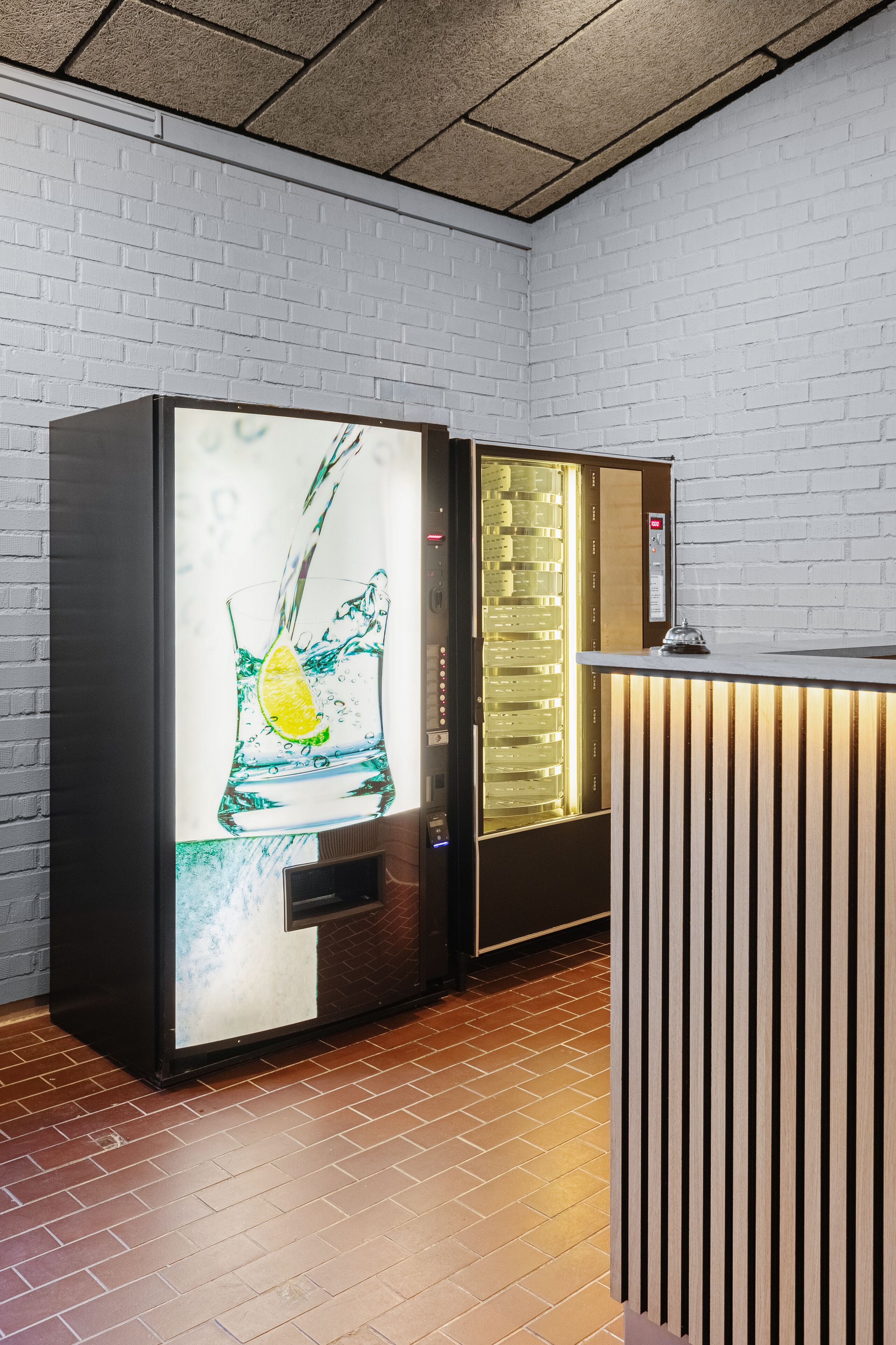 A modern hotel lobby with a brick wall, a reception desk, and a beverage dispenser.