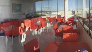 A dining area with red tables and chairs, large windows, and a view of the outside. - Hotel Mirante (Euclides Da Cunha)