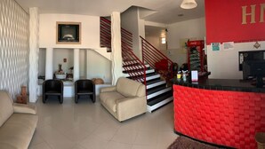 A living room with a sofa, two armchairs, a staircase with red railings, and a red reception desk. - Hotel Mirante (Euclides Da Cunha)