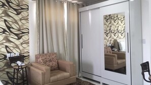 A room with a beige sofa, a small table, a white wardrobe, and a patterned wall. - Hotel Mirante (Euclides Da Cunha)