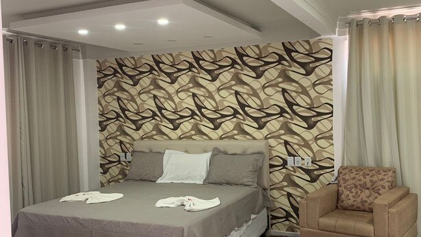 A bedroom with a bed, a chair, a patterned wall, and a fluffy rug. - Hotel Mirante (Euclides Da Cunha)