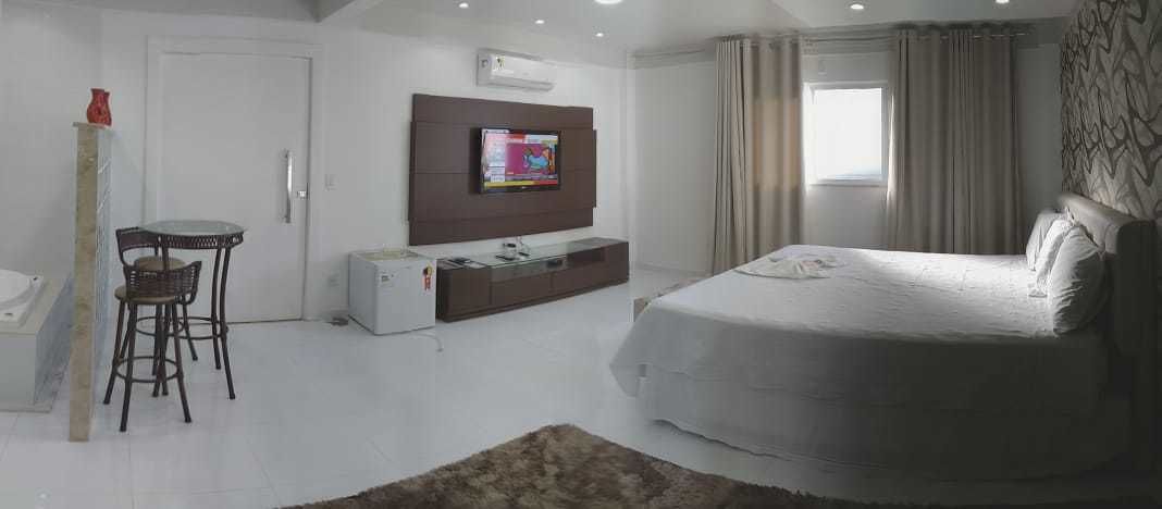 A bedroom with a bed, a TV mounted on the wall, a desk with a chair, and a window with curtains.