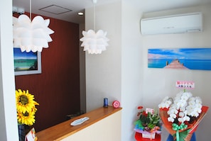 Un mostrador de recepción con encimera de madera, un jarrón con girasoles, un reloj y un cuadro de un muelle.