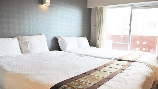 A hotel room with two beds, a large window, and a view of a building outside. - Ten Point Hotel (Naha)