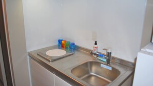 A stainless steel sink with a soap dispenser, a scale, and colorful glasses on a countertop. - Ten Point Hotel (Naha)