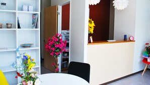 A reception area with a white reception desk, a black chair, and a white table with a floral arrangement. - Ten Point Hotel (Naha)