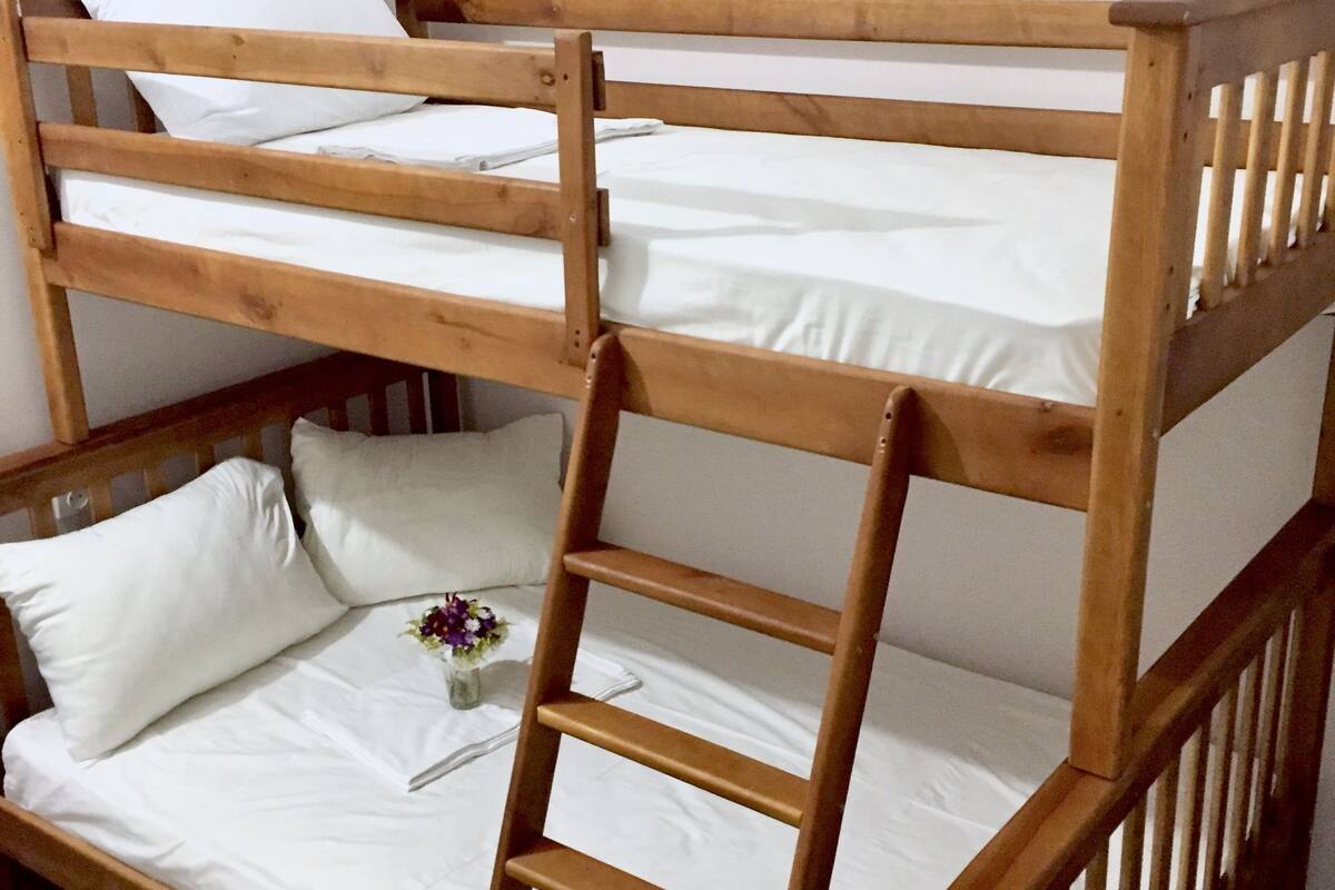 A bunk bed with a wooden ladder, white bedding, and a small vase with flowers on the lower bunk.