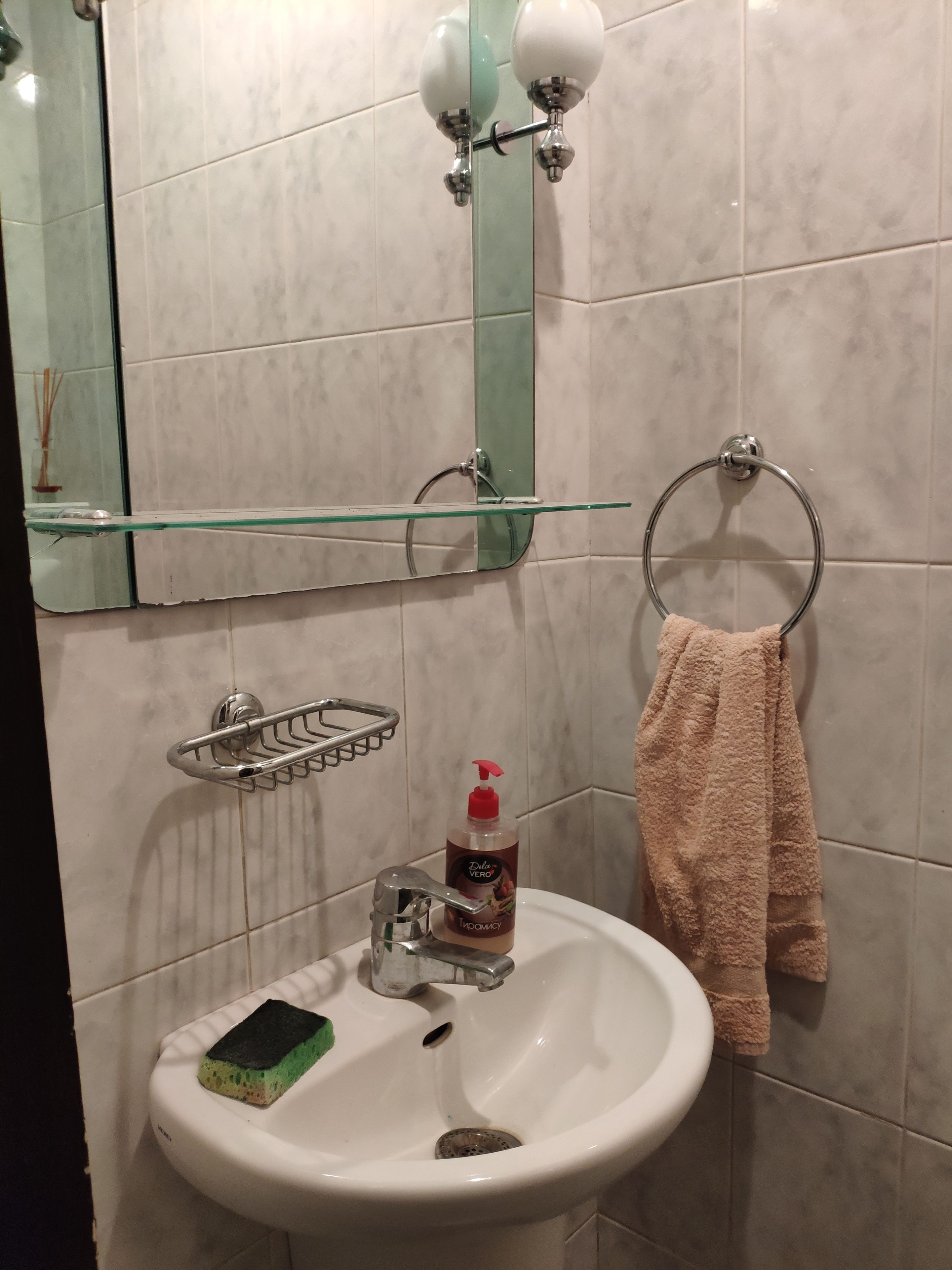Ein Badezimmer mit einem weißen Waschbecken, einer Glasablage, einem Handtuchhalter und einem Spiegel.