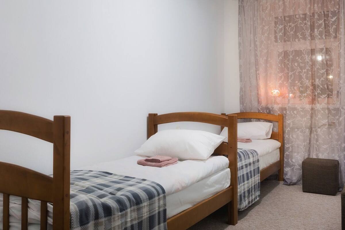 A small, clean room with two wooden beds, a small table, and a curtain.