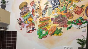 Una cocina con encimera de madera, dos taburetes y un mural que representa diferentes alimentos.